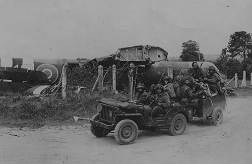 Glider pilots in a trailer being pulled by a jeep