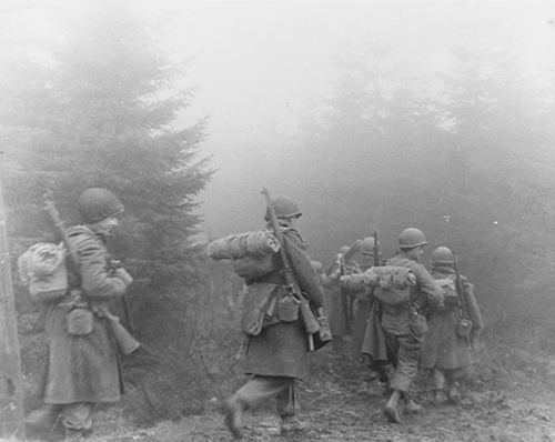 American soldiers advance through the forest of Ardennes