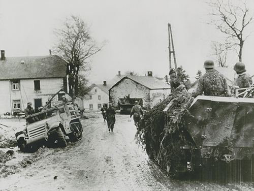 Waffen-SS Panzergrenadiers move past wrecked American truck